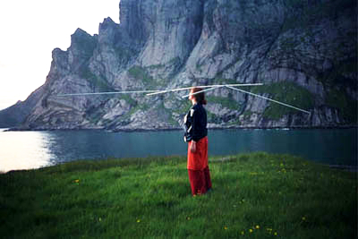 a person is standing in a mountainous setting balancing an antenna on its head